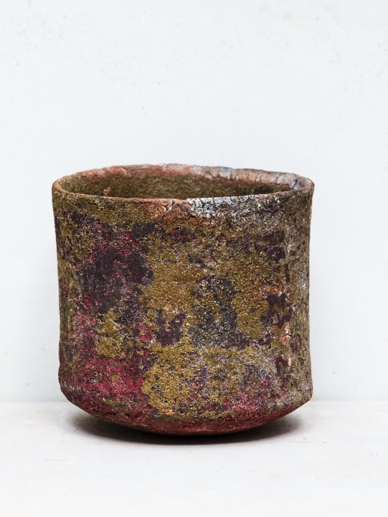 Dunkelbrauner Stoneware-Becher mit rauer Textur auf hellem Untergrund