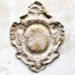 Patinierte steinerne Rosette in Wappenform auf hellem Grund