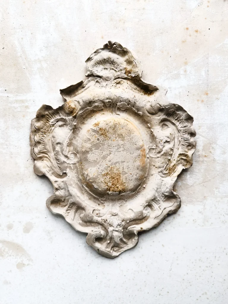 Patinierte steinerne Rosette in Wappenform auf hellem Grund