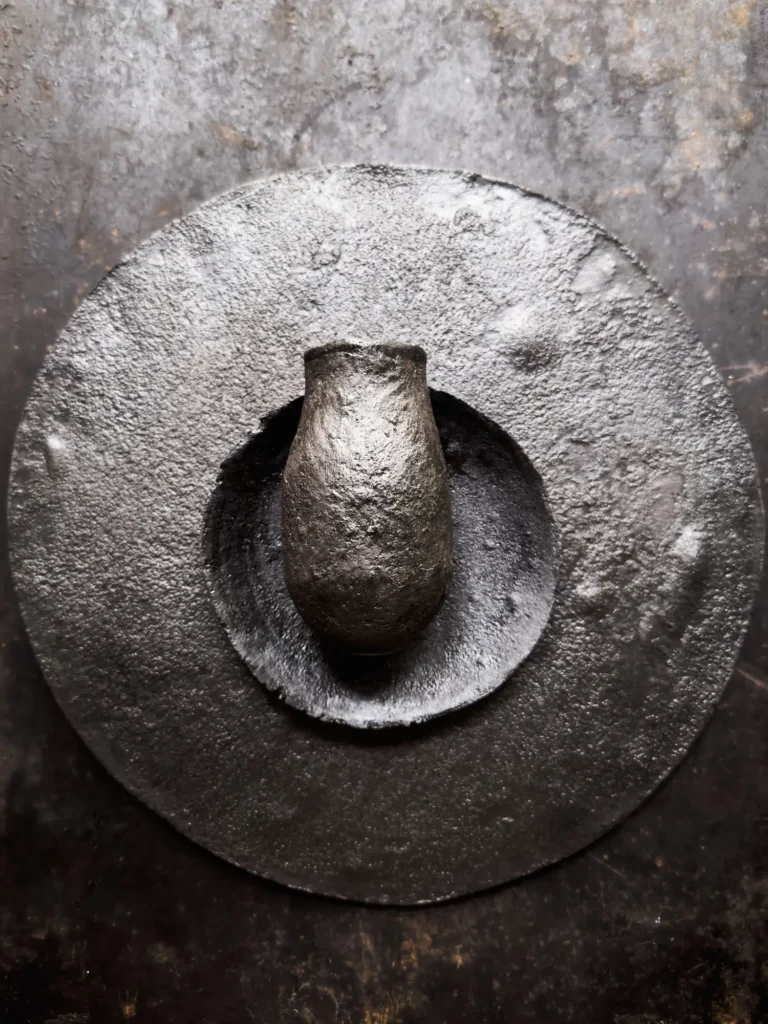 Arrangierte Stoneware-Vase, aufliegend auf Stoneware-Tellern, gräulich patiniert, aufgenommen vor grauem Hintergrund