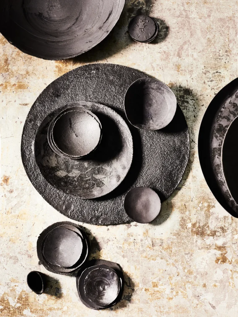 Arrangierte schwarze Lava-Stoneware-Schalen und Tassen von Dietlind Wolf auf hellem Hintergrund