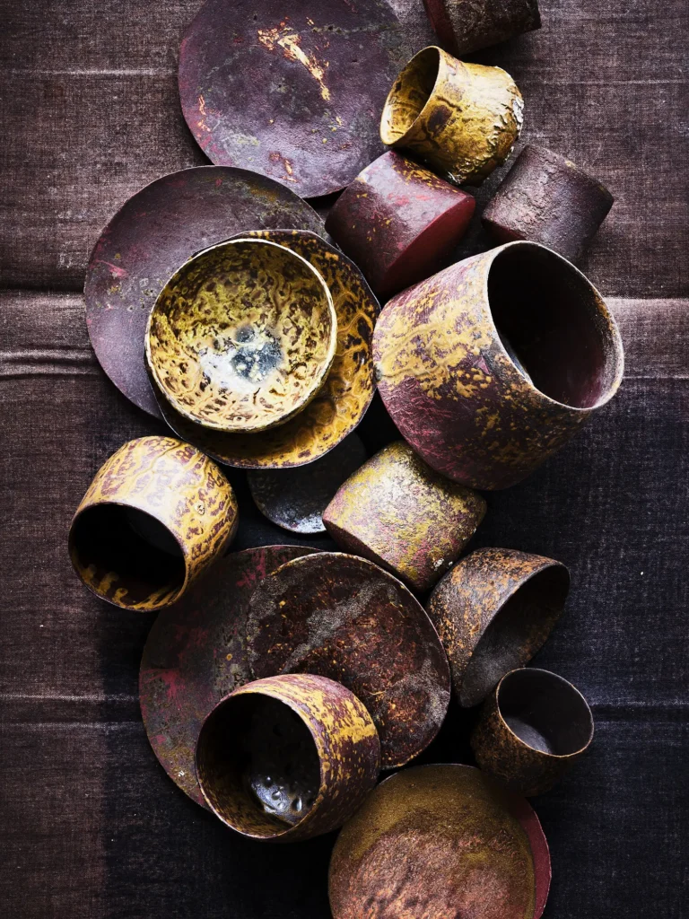Vertikale Anordnung Stoneware-Schalen, Teller und Becher mit oxidierter Erdpigment-Patina