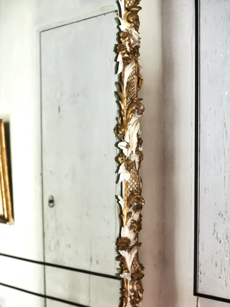 Detail eines verzierten Spiegelrahmens mit floralen Ornamenten in Gold und Weiß.