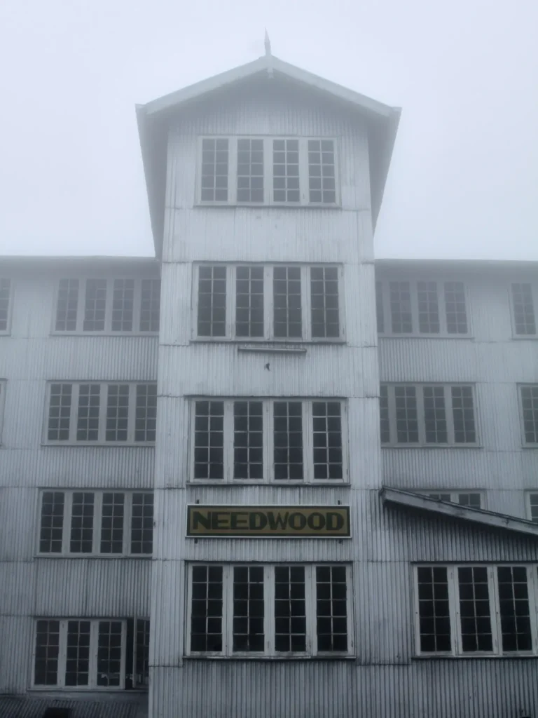 Nebliges Industriegebäude mit symmetrischer Fassade und Schriftzug ‚Needwood‘