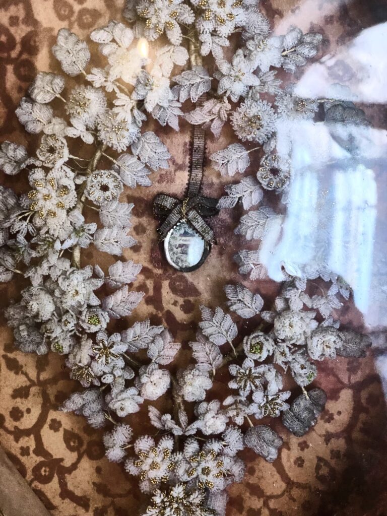 Kranz aus filigranen Blüten mit kleinem Anhänger auf gemustertem Untergrund.