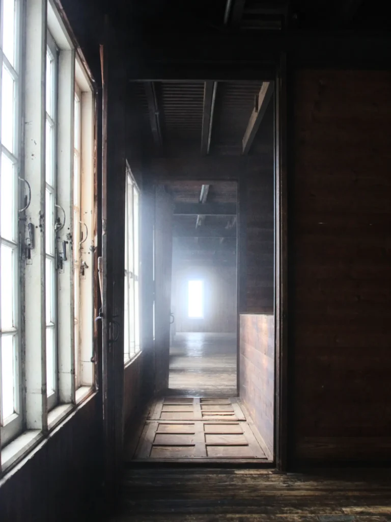 Leerer Innenraum mit Holzboden, Fensterfront und Licht am Ende eines Flurs.