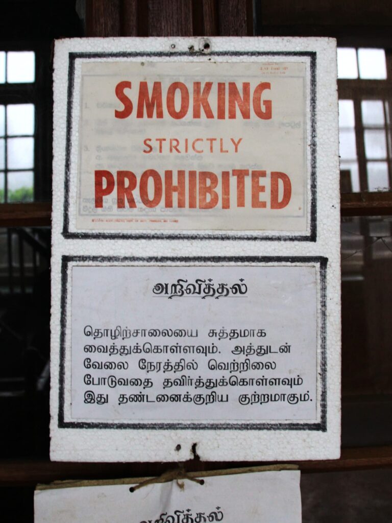 Hinweisschild mit der Aufschrift ‚Smoking strictly prohibited‘ und zusätzlichem Text in tamilischer Schrift.