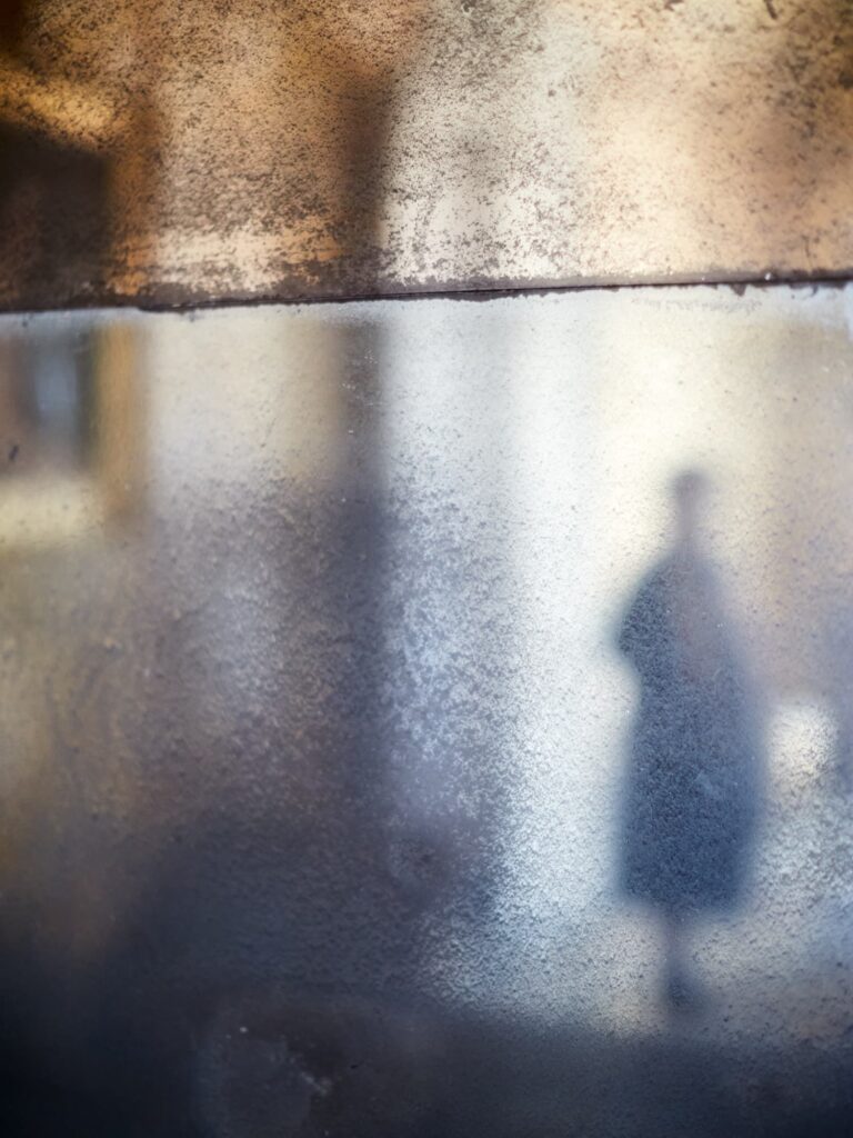 Schemenhafte Person hinter strukturierter Glasfläche mit Licht- und Schatteneffekten.