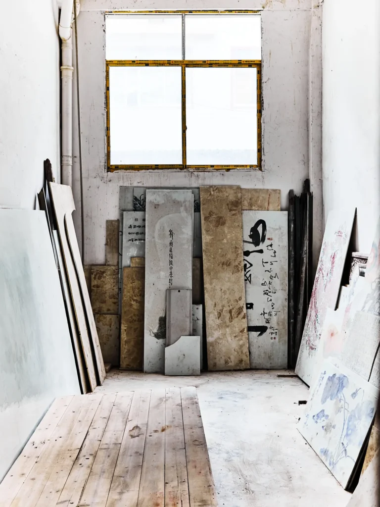 Werkstattraum mit hohem Fenster; an den Wänden lehnen verschiedene Stein- und Marmorplatten mit Schrift- und Farbspuren, der Boden ist hell und staubig.