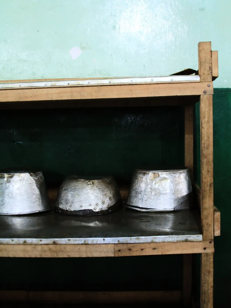 Metallregal aus Holz mit drei abgenutzten Aluminiumtöpfen, umgedreht auf einer Metallablage vor einer grün gestrichenen Wand.