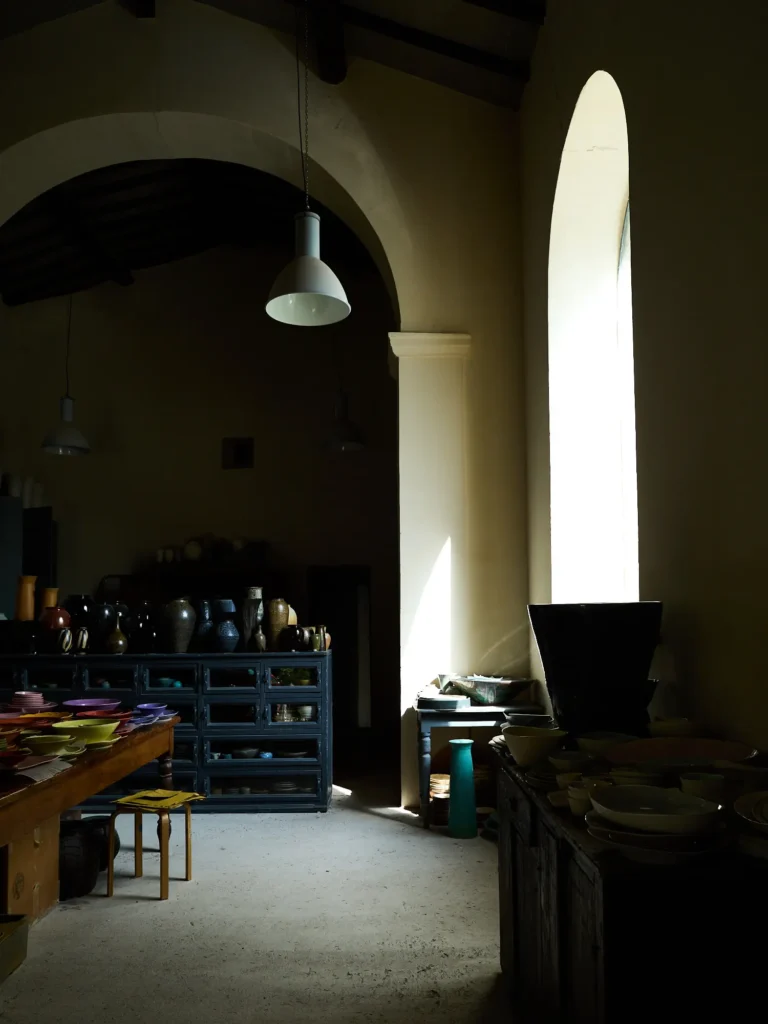 Lichtdurchflutete Keramikwerkstatt mit hohen Bögen, Regalen voller Gefäße und Arbeitstischen
