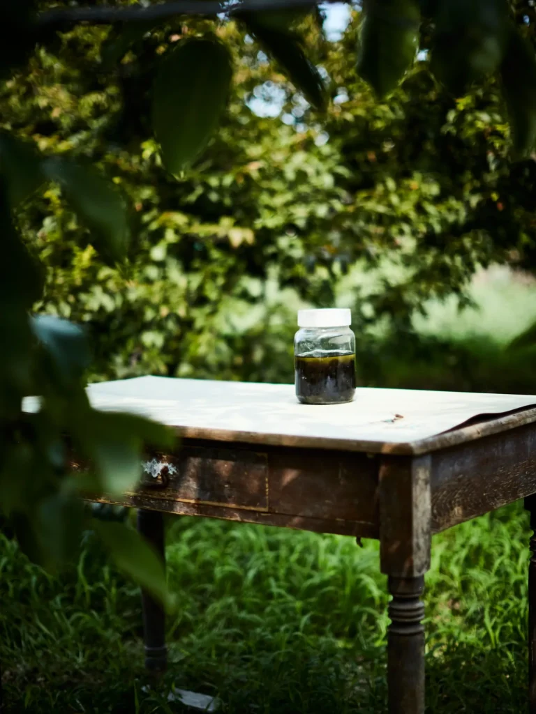 Glas mit dunkler Flüssigkeit steht auf einem Holztisch im Garten.