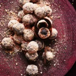Dunkle Bliss Balls in einer rötlichen Keramikschale, bestreut mit grünen Pistazienkernen und rötlichen Gewürzen.