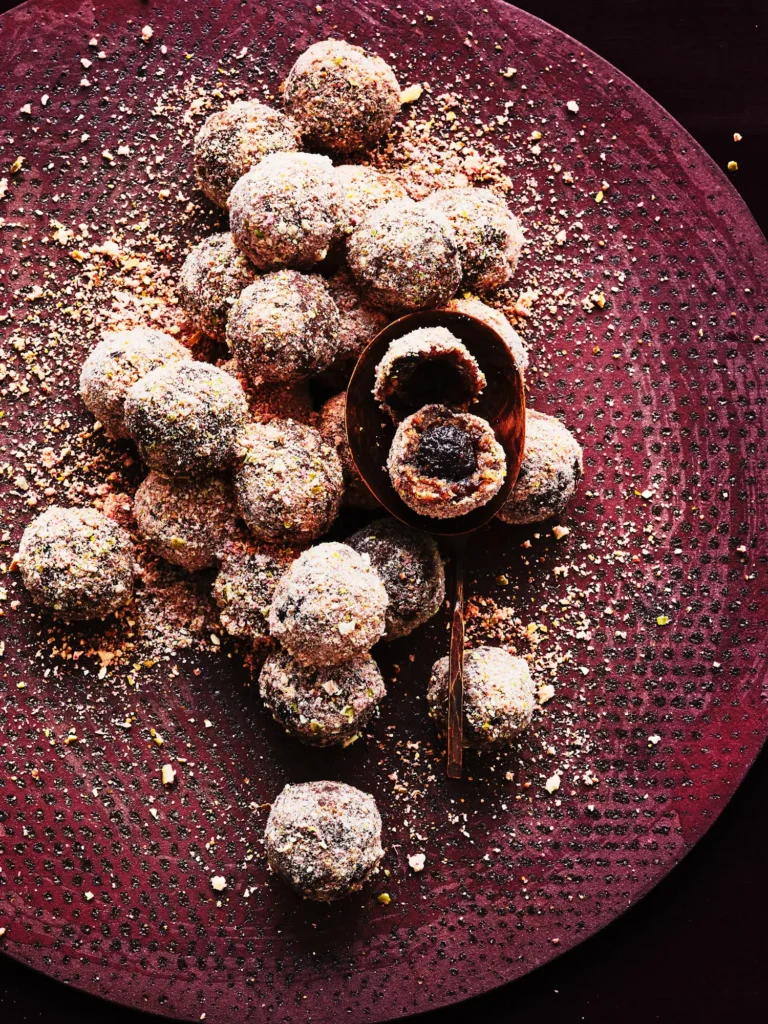 Dunkle Bliss Balls in einer rötlichen Keramikschale, bestreut mit grünen Pistazienkernen und rötlichen Gewürzen.