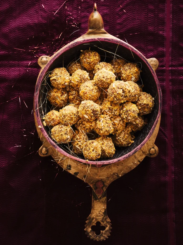 Kleine Blissballs, gewälzt in Curry, in einem gelblichen Schale, geschmückt mit Gewürzfäden auf weinrotem Hintergrund