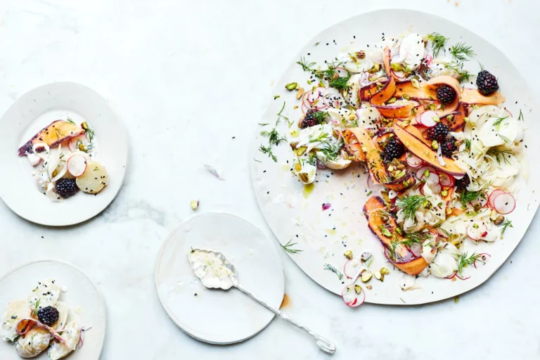 Moderner Kartoffelsalat auf hellen Tellern, garniert mit violetten Karottenstreifen, Radieschen, Brombeeren, Dill und gehackten Pistazien auf einer Marmoroberfläche.