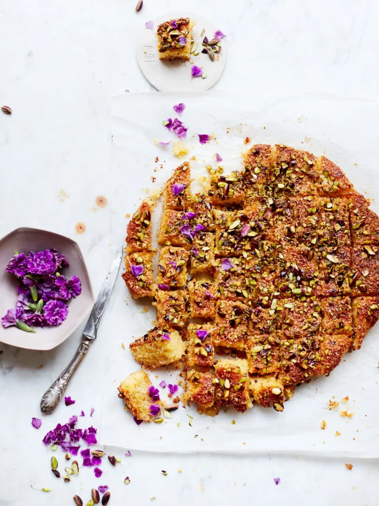 Saftige Quadrate von Joghurtkuchen, garniert mit Kokosraspeln, gehackten Pistazien und violetten Blütenblättern.